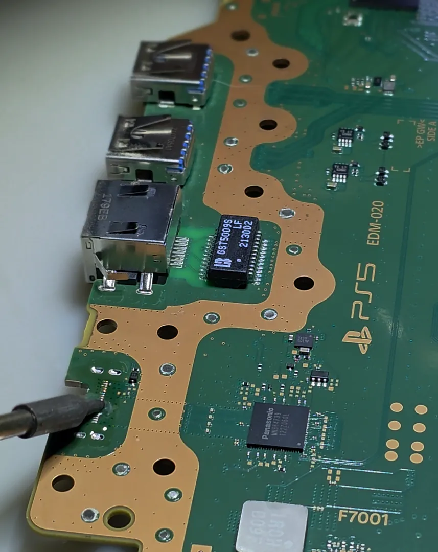 Fer à souder en action sur la carte mère d'une PS5, à côté des ports USB.